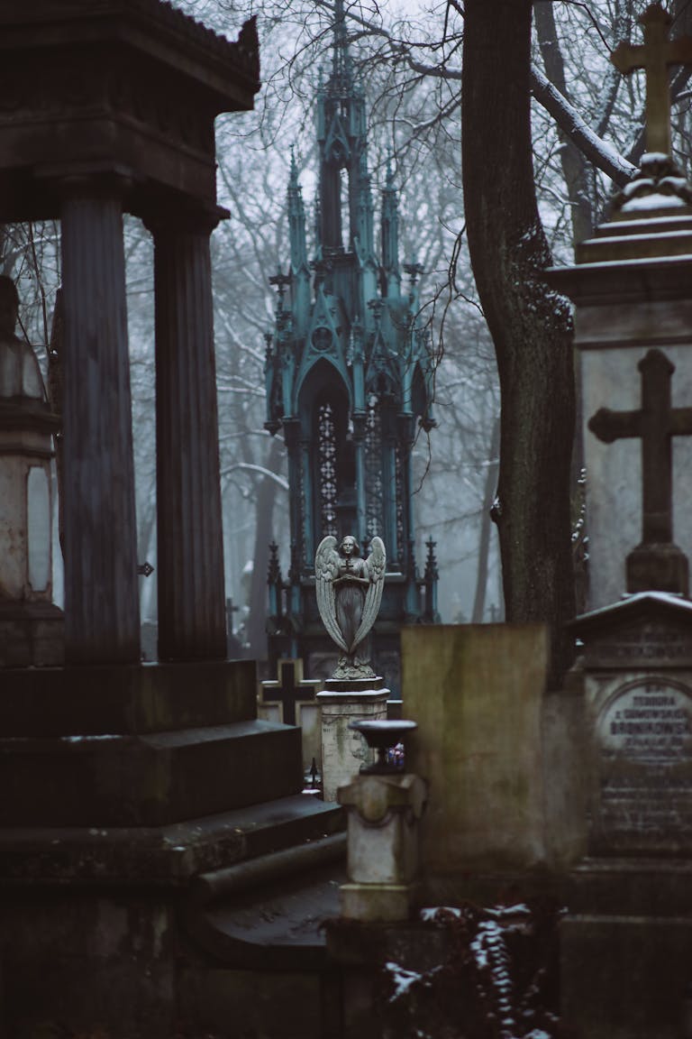 A moody cemetery shrouded in fog featuring gothic tombstones and angel statues.