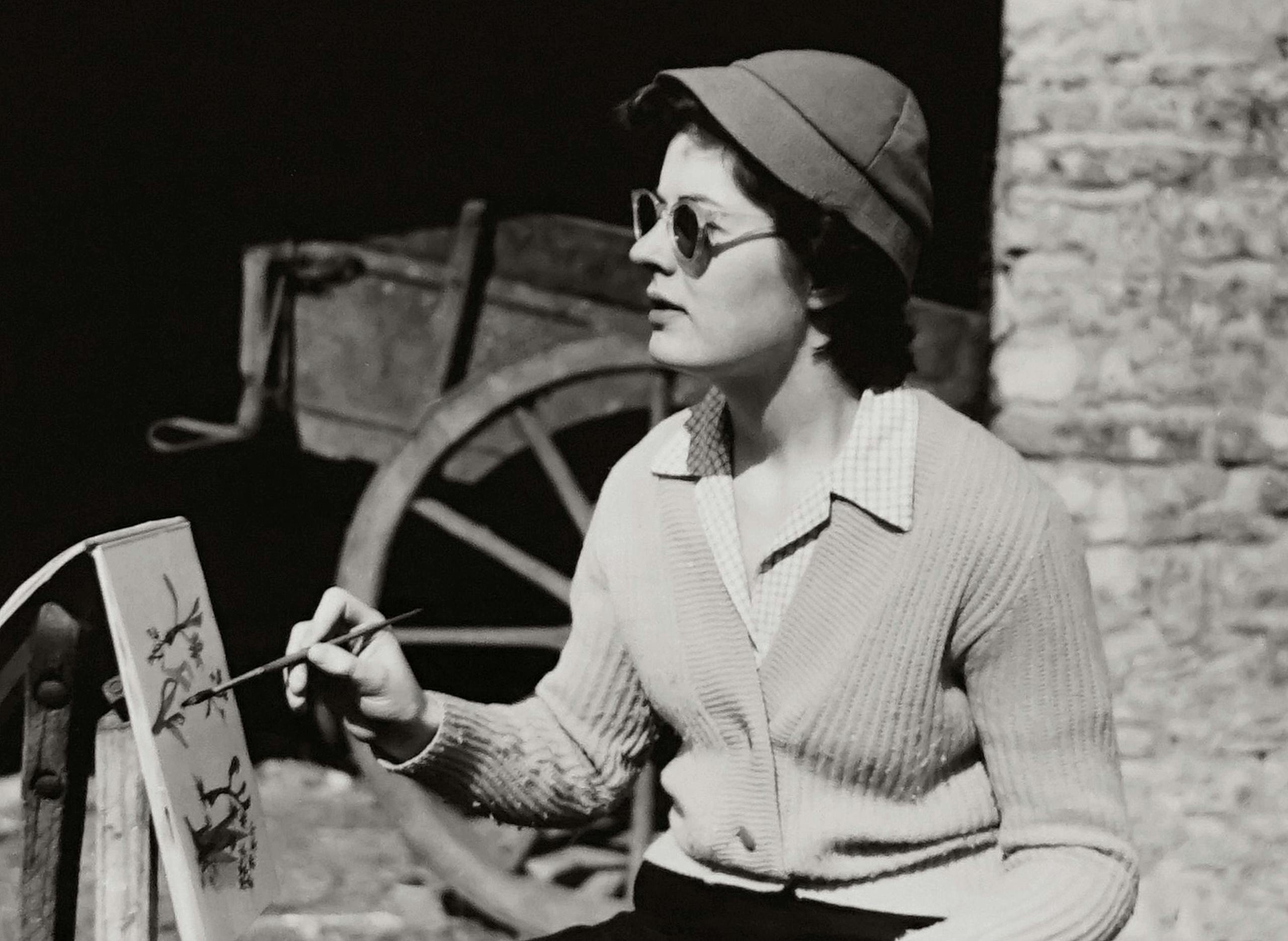 Czarno-białe zdjęcie retro kobiety malującej na zewnątrz, z okularami przeciwsłonecznymi i swetrem – sztuka i wspomnienia