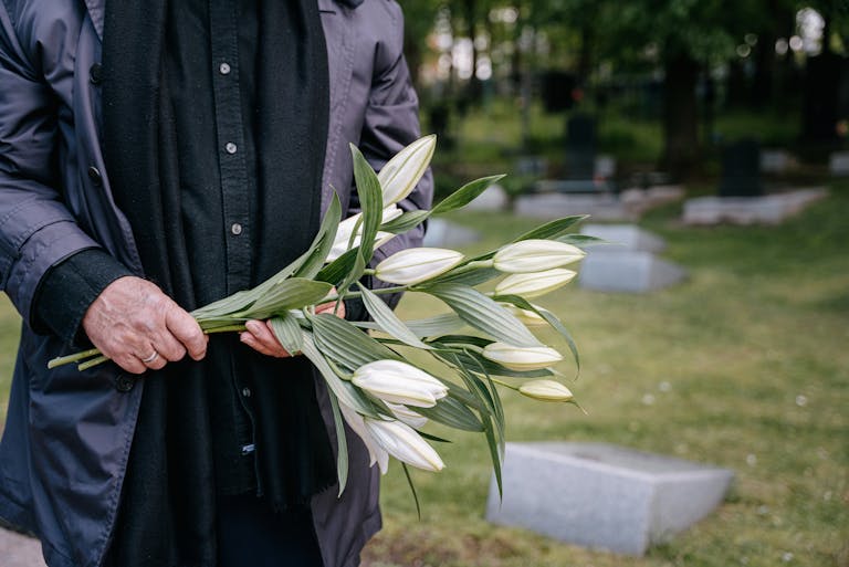 Close-up of a person holding white lilies in a cemetery on a peaceful day.