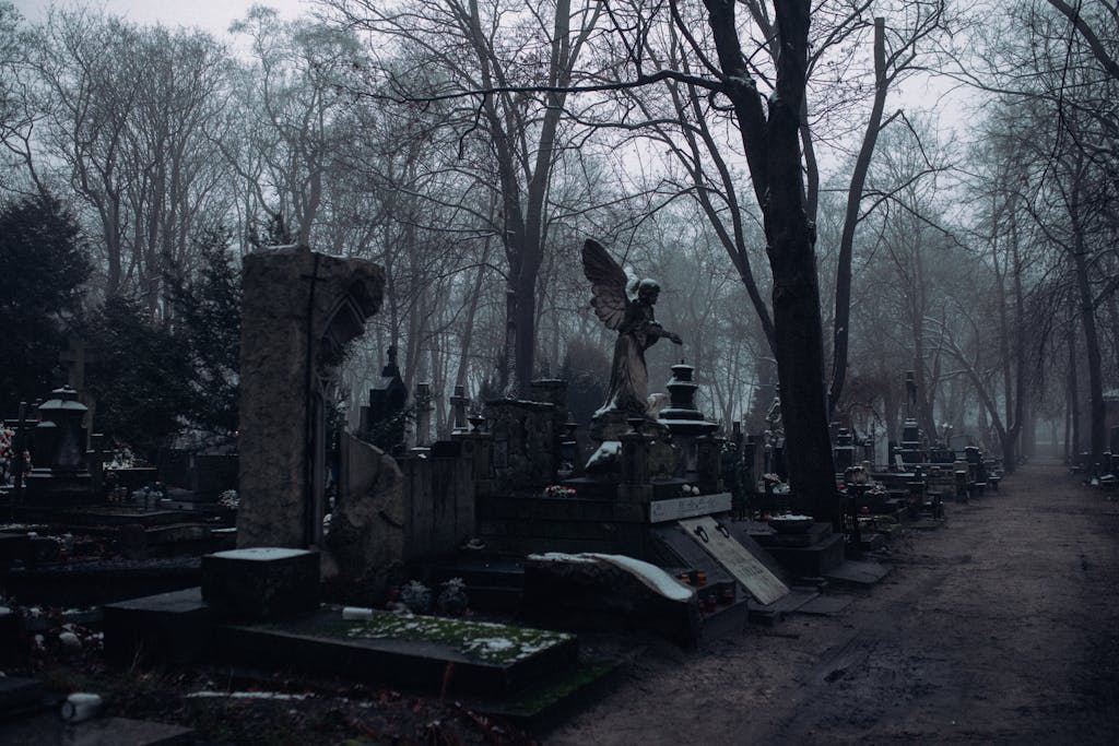 Foggy cemetery scene with bare trees and tombstones creating a somber and mysterious atmosphere.